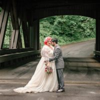plus size bride holding flowers, groom on a wooden bridge